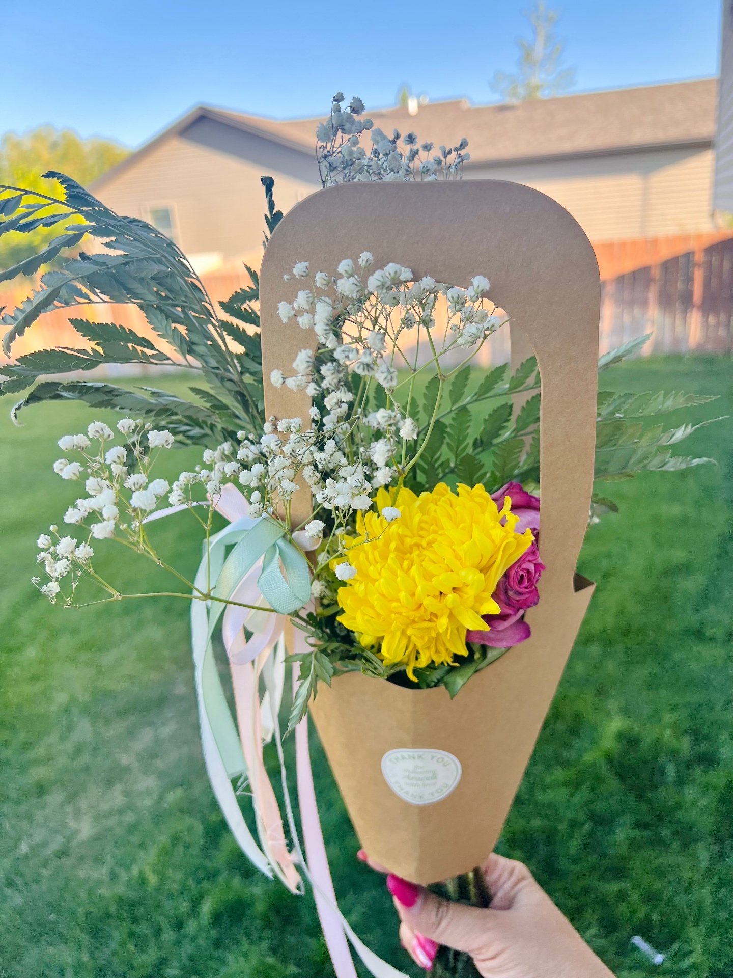 Guest holding a finished bouquet with yellow mum, pink rose, and baby's breath in kraft wrap